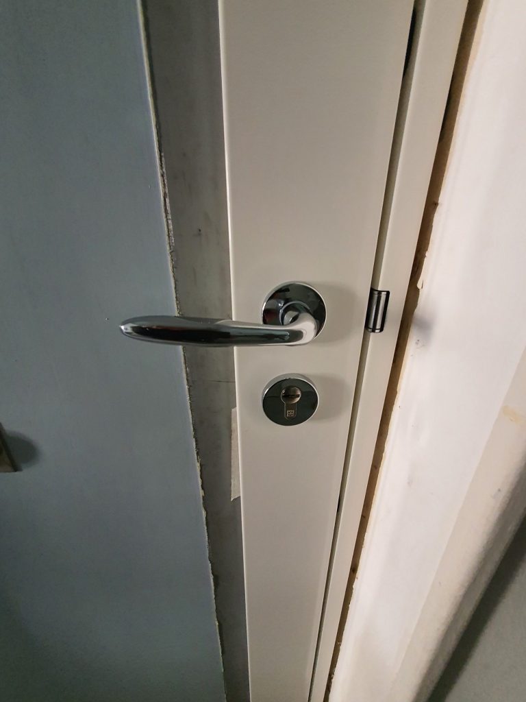 Poignée de porte métallique avec serrure sur un mur blanc.